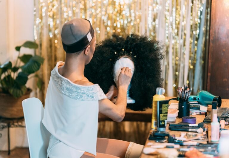 A person styles a wig in a vibrant dressing room with makeup and tools.